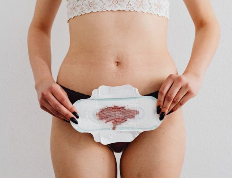 A woman holds a menstrual pad demonstrating feminine hygiene in an indoor setting.